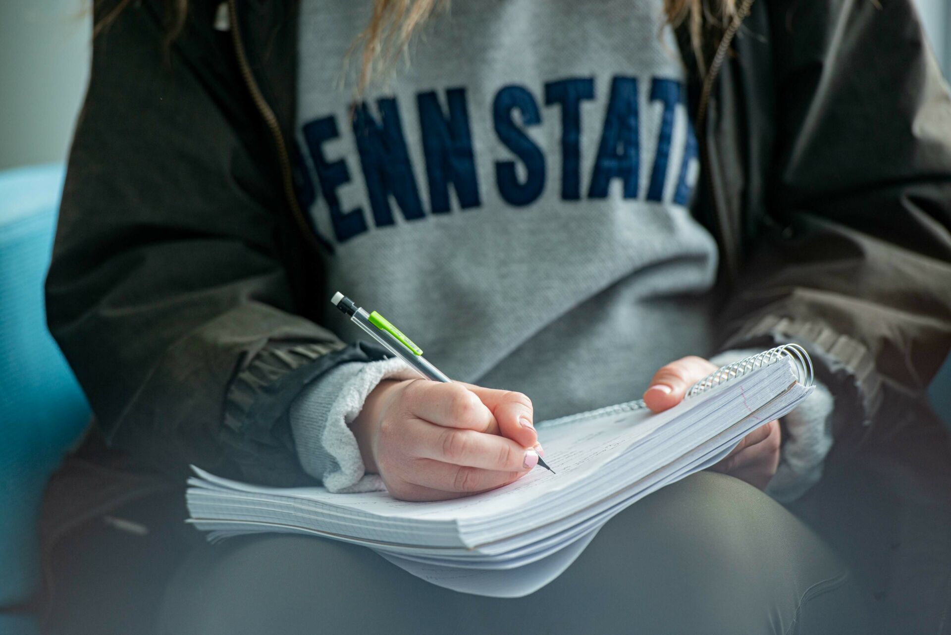 Student in a Penn State sweatshirt writing in a notebook