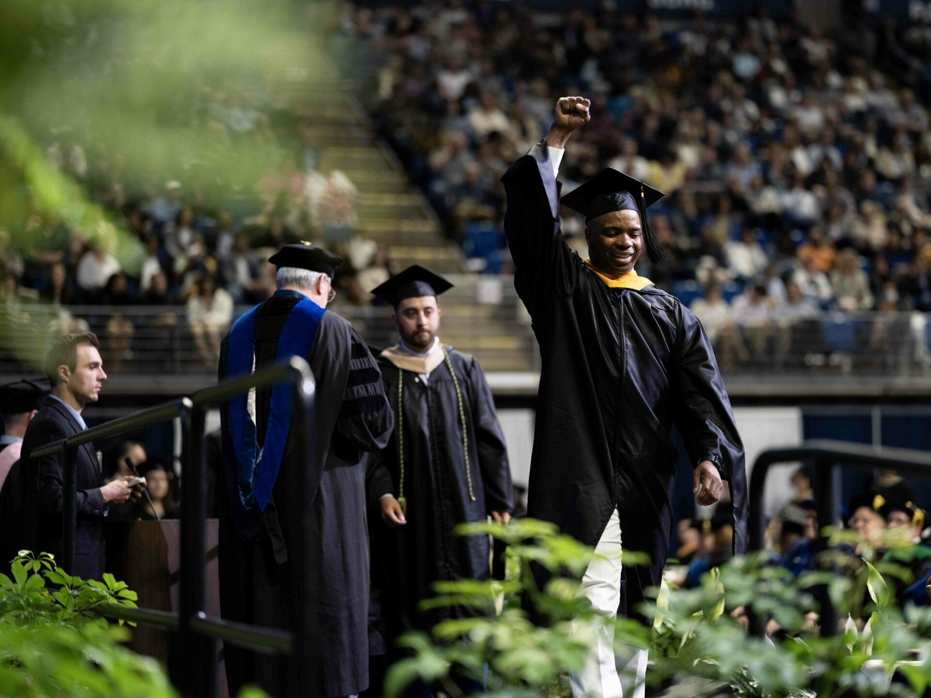 student crossing stage at commencement with hand raised in the air