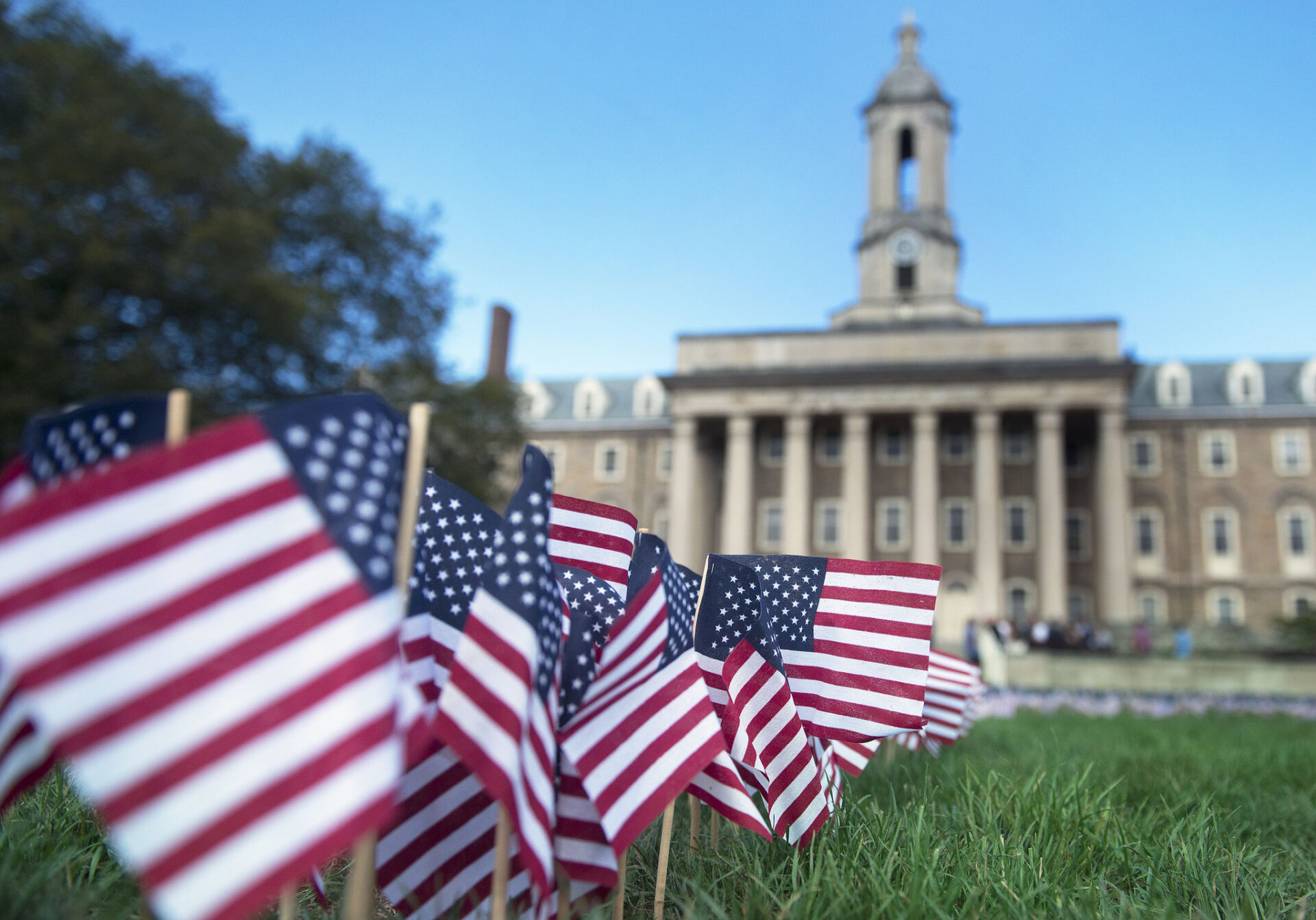 A cluster of small American flags on the lawn of Old Main in focus in the foreground; Old Main in the distance.