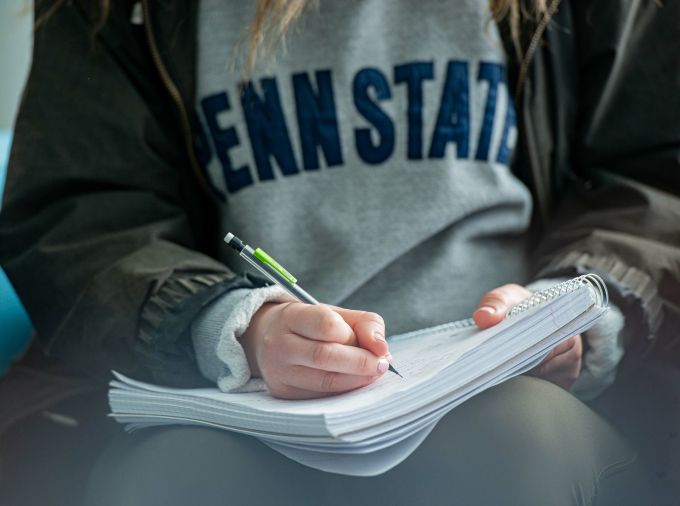 Student in a Penn State sweatshirt writing in a notebook