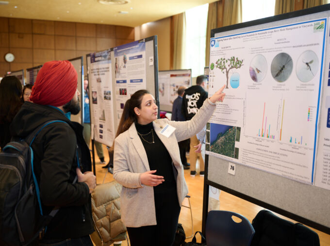 A graduate student presents their poster presentation to a judge at the annual Graduate Exhibition in Alumni Hall of the HUB-Robeson Center.