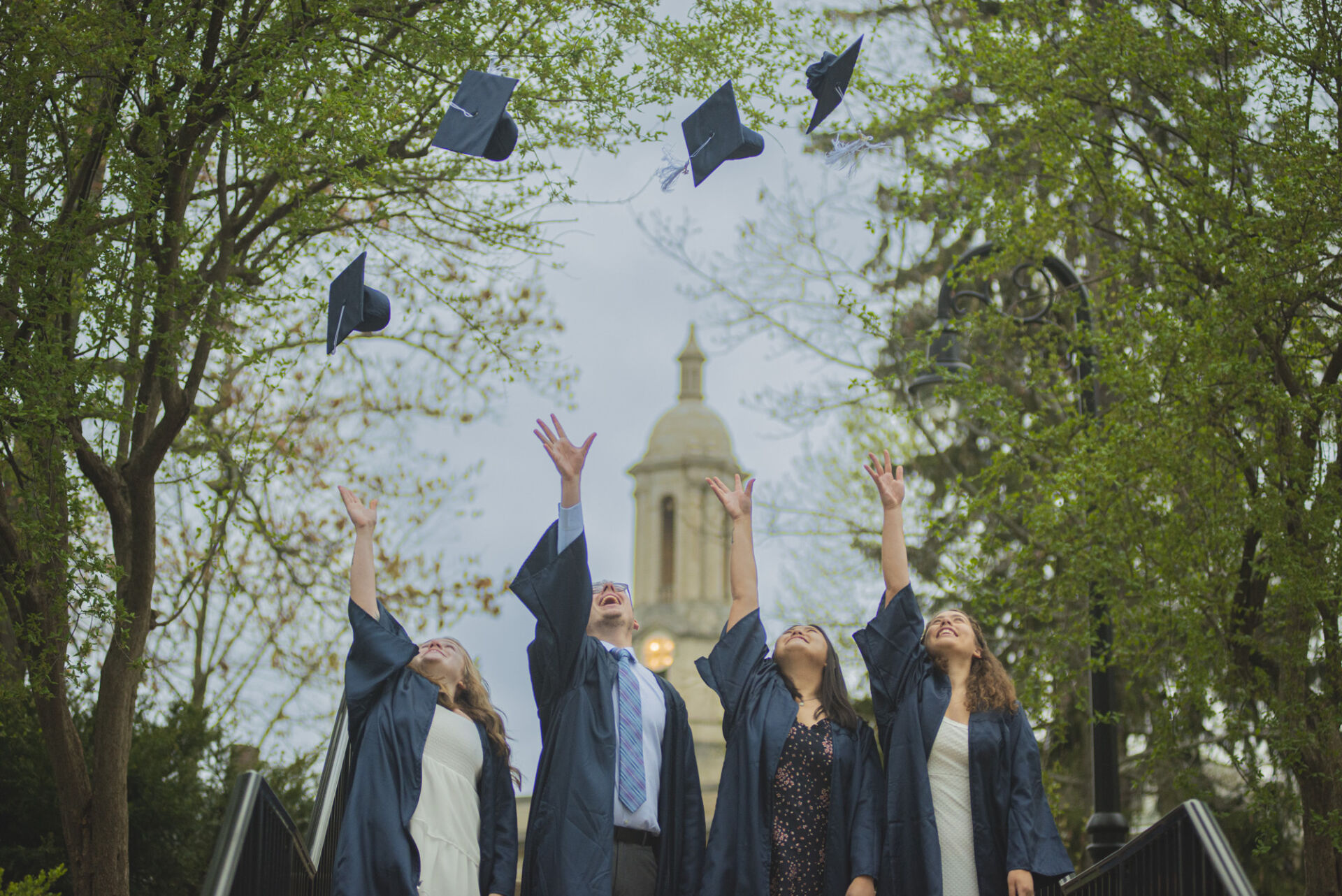 Recent graduates in robes tossing their hats into the air in front of Old Main.
